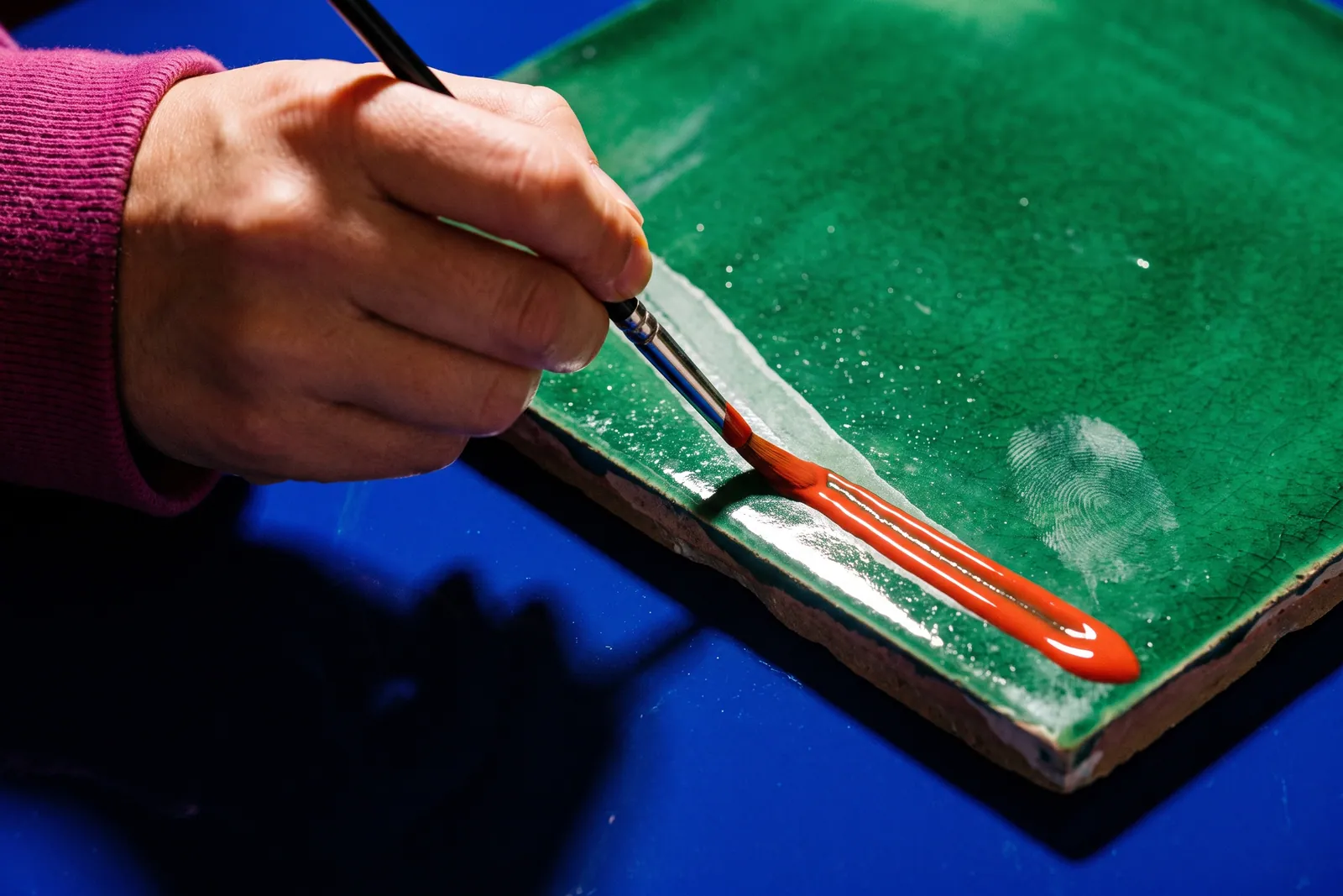 A close, low-angle view of a designer's desk: a screen showing a type specimen in progress, a printed proof marked up in pencil beside it, and a hand adjusting the spacing.